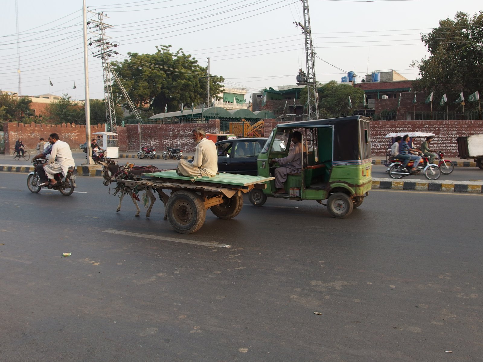 A donkey pulling a wooden cart carrying a seated man alongside other road traffic.